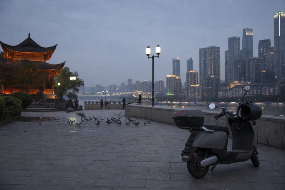 Scooter parked on a lit riverside promenade with a glowing skyline across the water