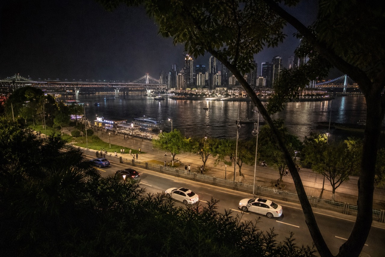 Night view across a wide river toward a dense skyline of illuminated towers and bridges