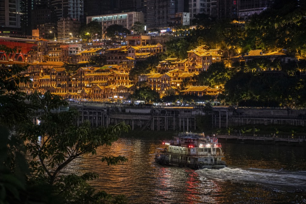 Traditional stilt-house architecture of a riverside Chongqing landmark lit warmly at night above the water