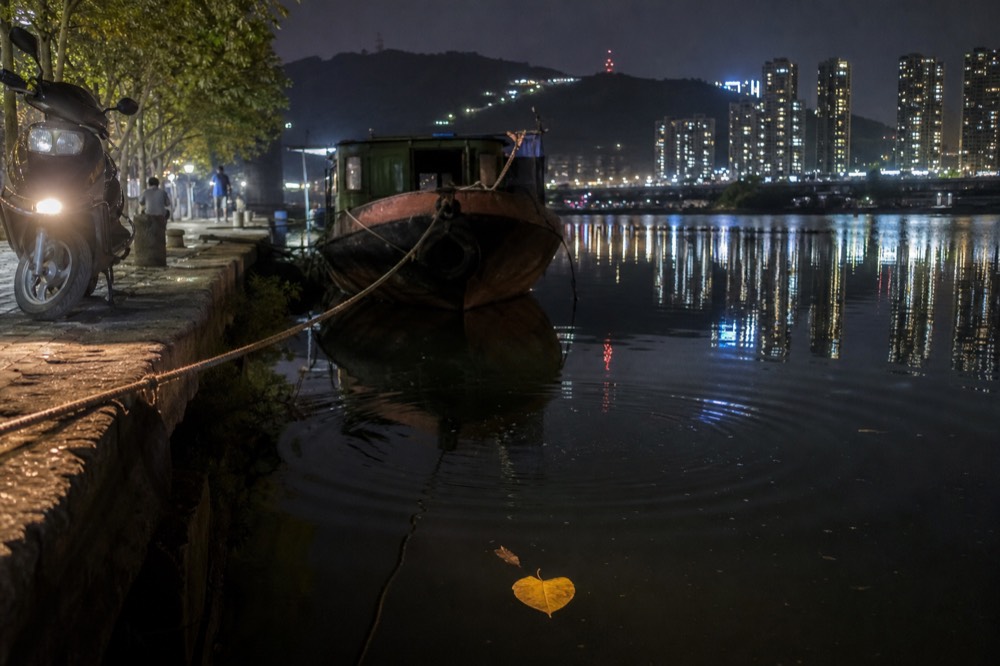 A motorcycle headlight and lit tower blocks reflected in a wide river at night