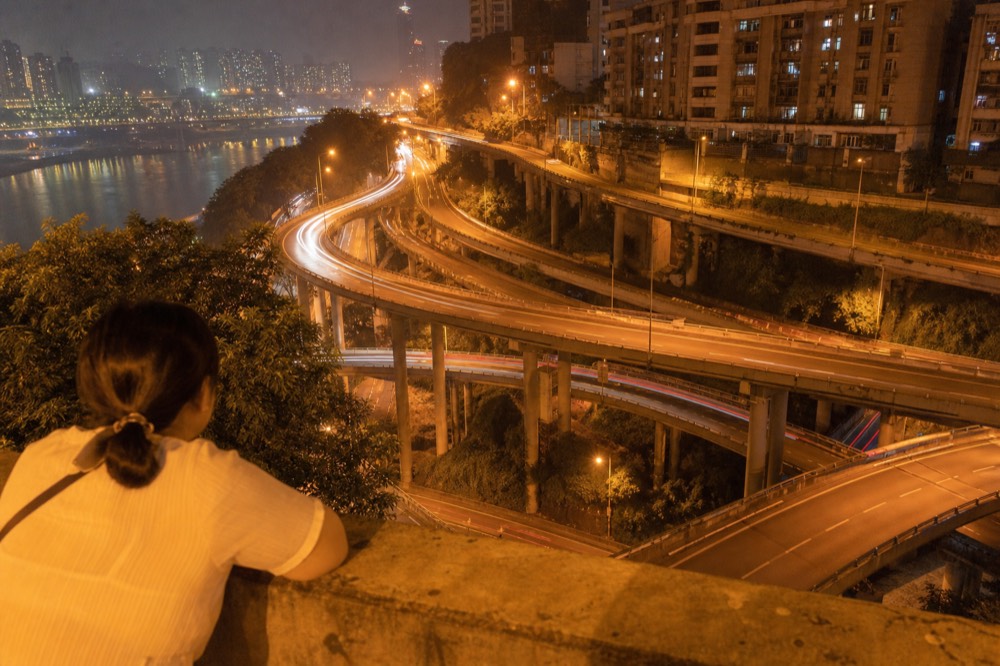Multi-level elevated roads winding between hillside apartment towers in Chongqing at night
