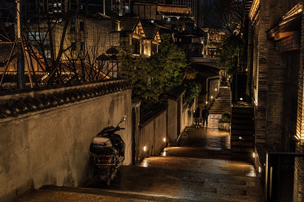 Steep city streets stacked on a hillside at night with buildings rising at different levels