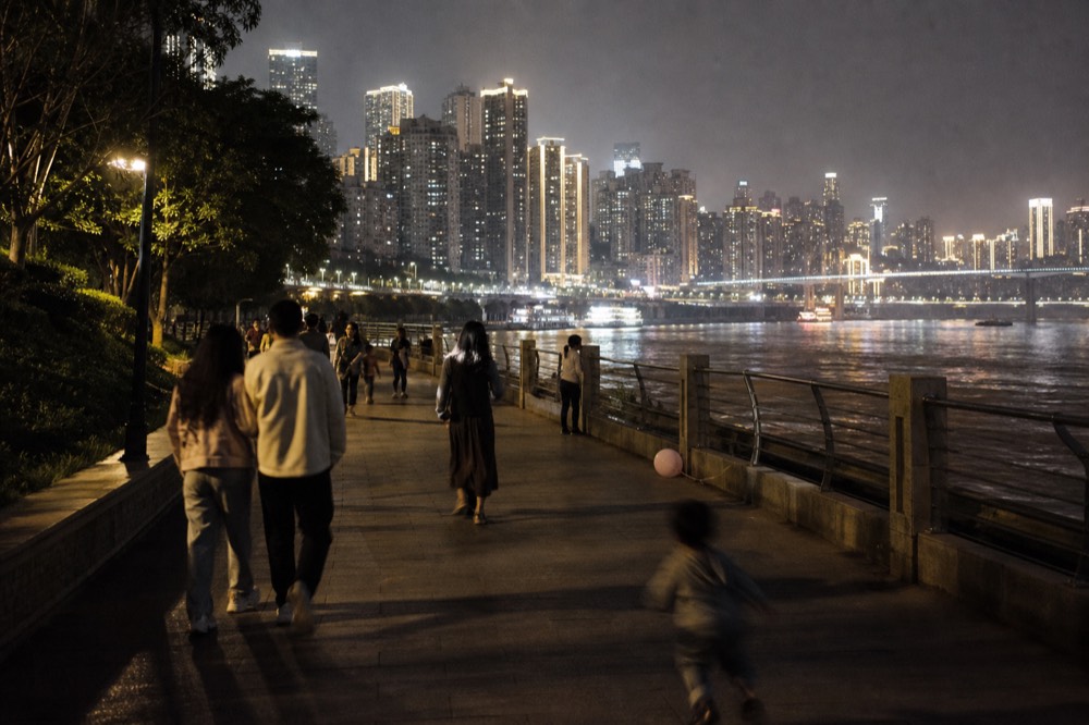 Crowded riverside promenade with lit towers across the water at night