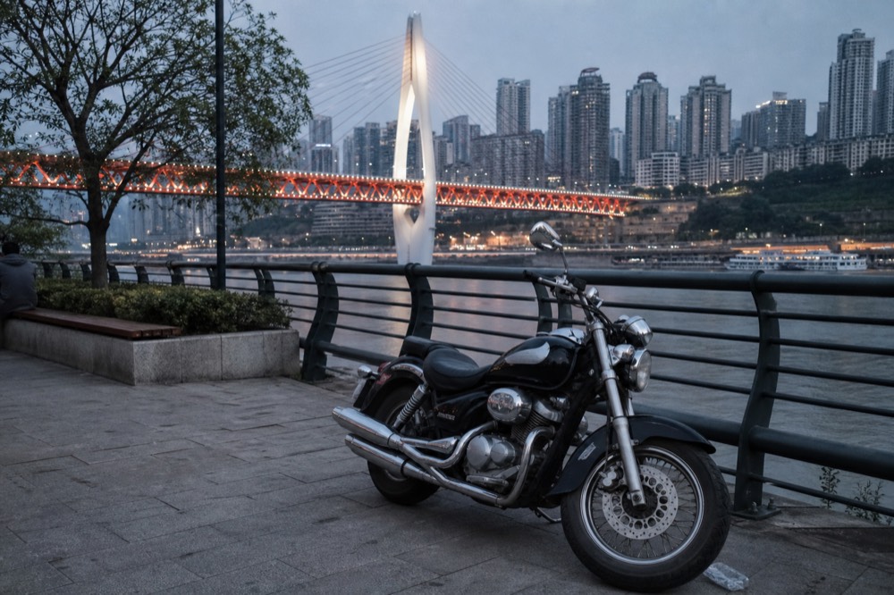 Motorcycle parked beside a river railing with lit bridge towers behind