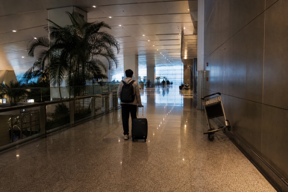 Traveller walking through an airport corridor with a backpack toward the light