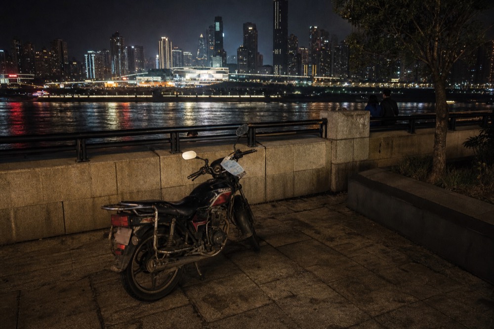 Motorcycle parked on a riverside promenade with illuminated towers across the water at night