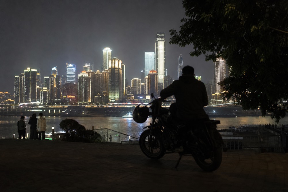 Motorcycle and rider silhouetted against a brightly lit riverside skyline at night
