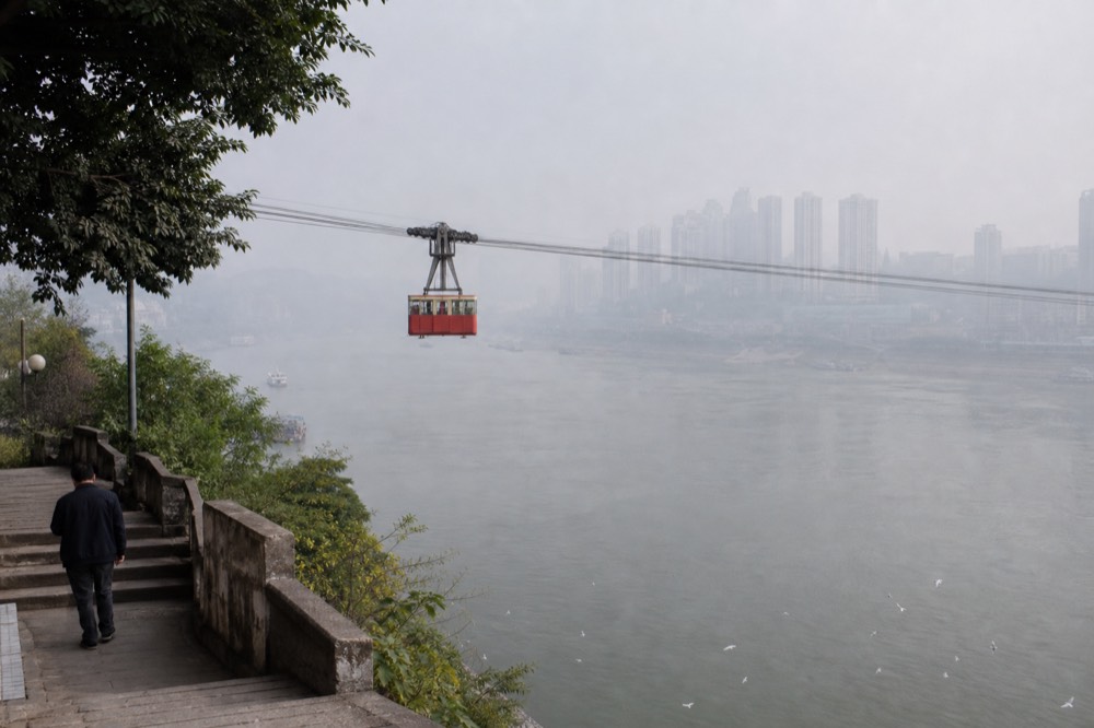 Aerial cablecar cabin suspended above a wide river between city districts