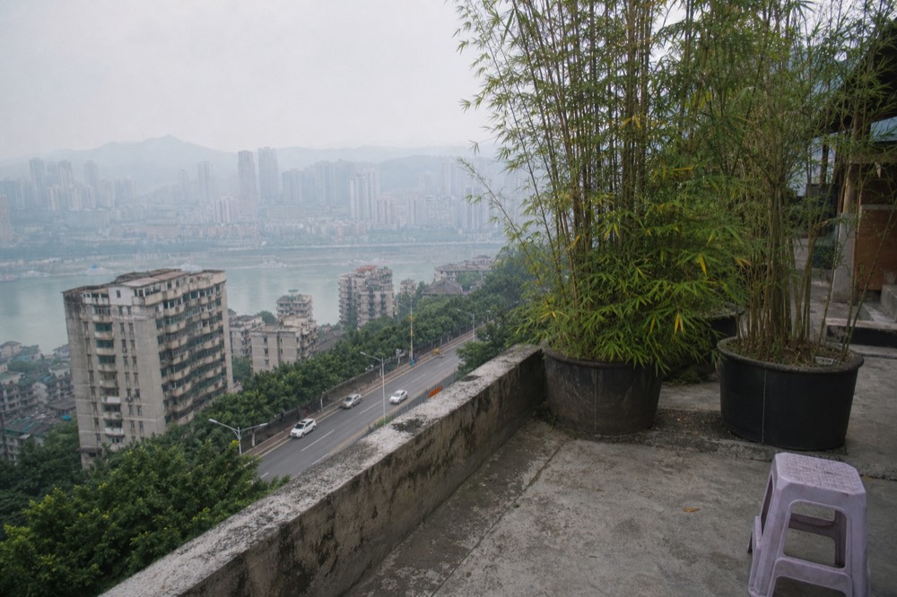 Weathered rooftop terrace with potted bamboo overlooking a hazy Chongqing morning
