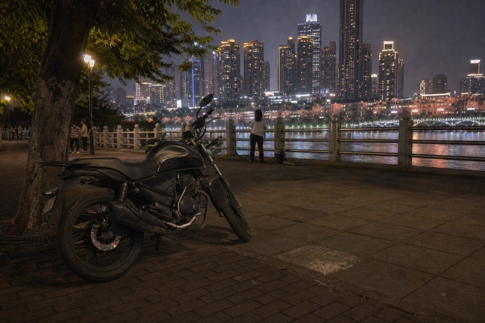 Parked motorcycle under night lights with a city skyline glowing across a river