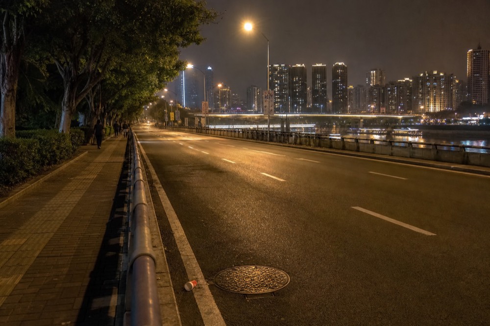 Empty riverside boulevard at night with road markings visible and city lights beyond