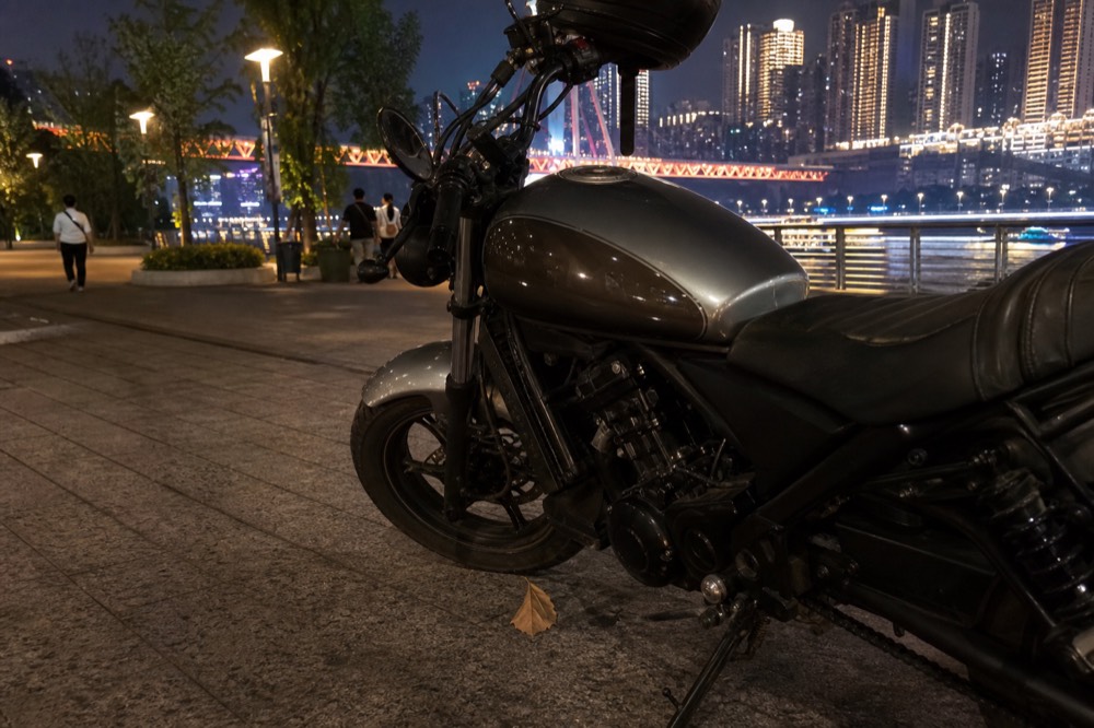 A motorcycle parked on a night street with a glittering city skyline and river bridges glowing in the background.
