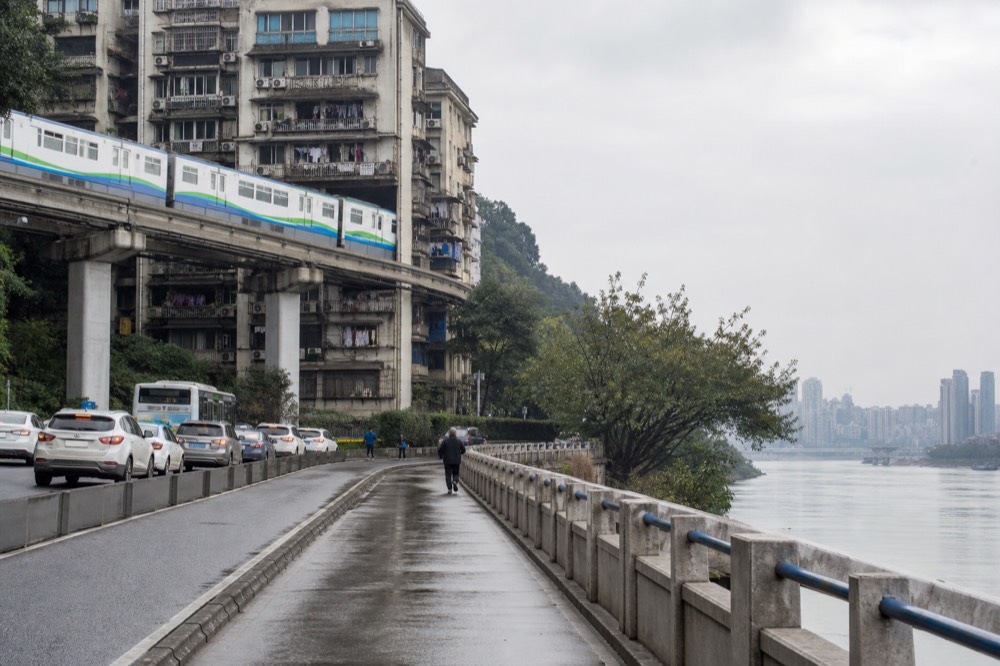 A monorail train passing through the middle floors of a residential building above a city street.
