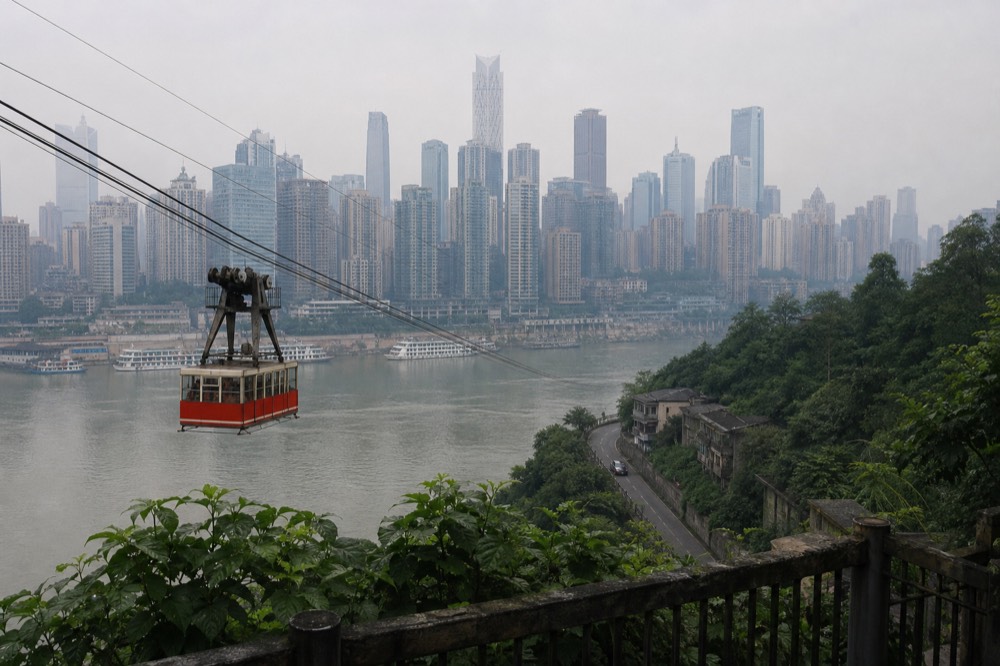 Aerial tramway cabin suspended on cables above a wide river with a lit city skyline in the background