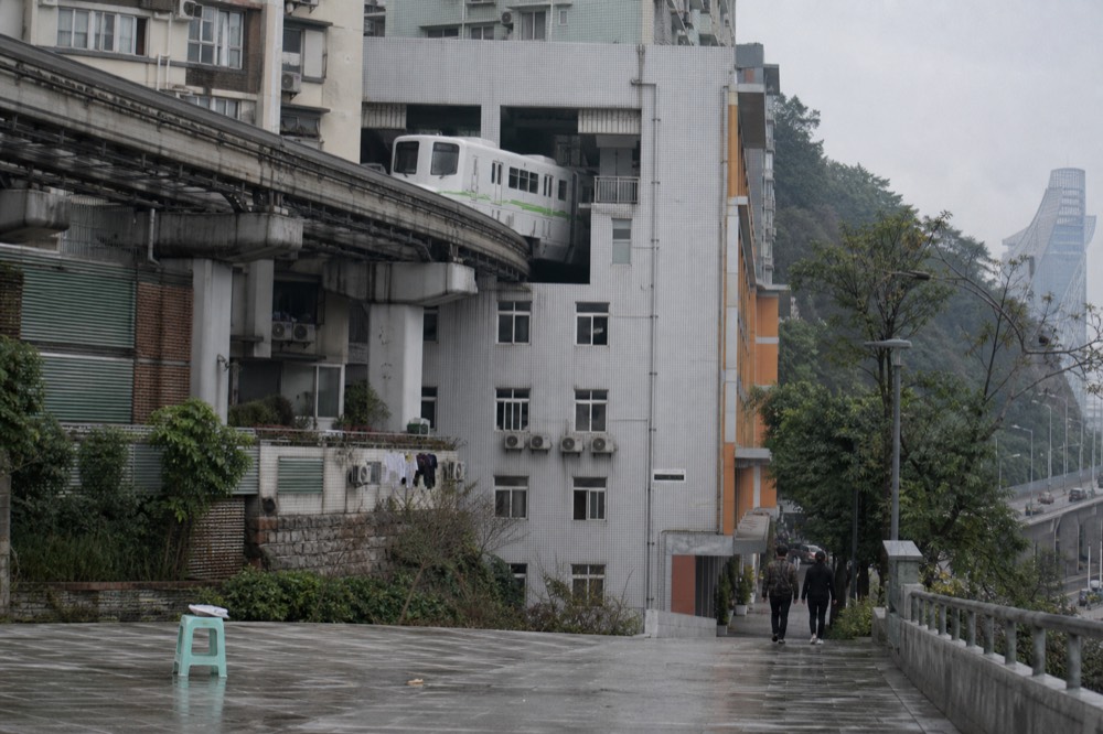 A monorail train emerging from an opening in the side of a high-rise residential building above a city street