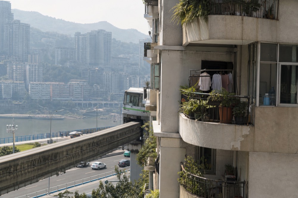 A single-track monorail beam passing between residential balconies on the middle floors of a tower