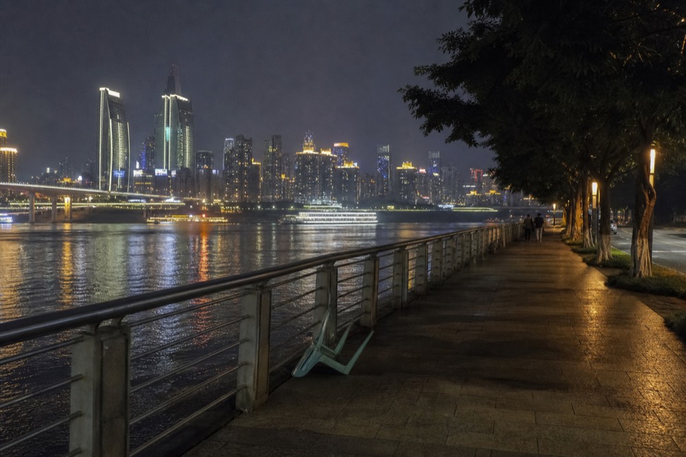Lit riverside promenade at night with the skyline of the opposite bank reflected in the wide river