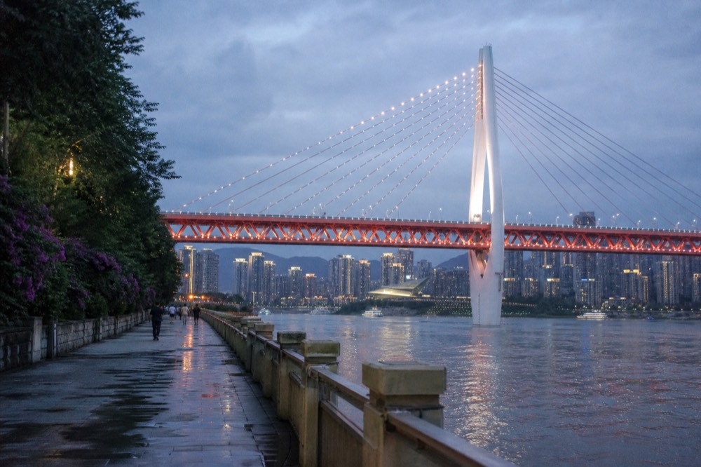 Cable-stayed bridge lit at night spanning a wide river, with towers glowing on the far bank