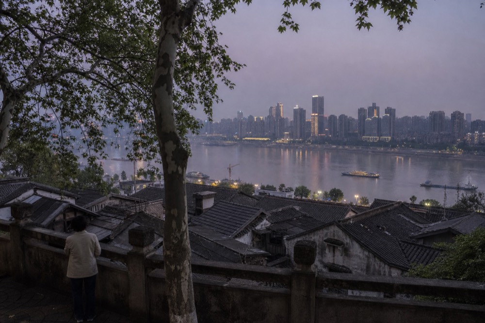 Hilltop park viewpoint at dusk looking across rooftops toward a river and lit towers beyond